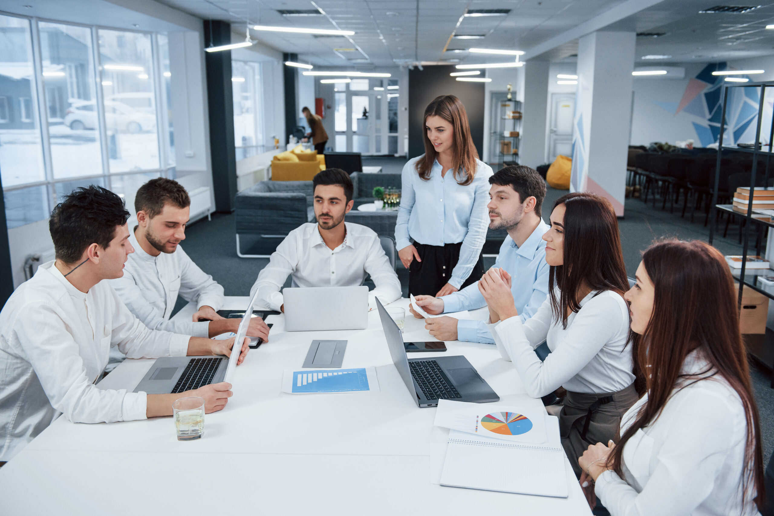 Guy on the left side talking and colleagues is listening to him. Group of young freelancers in the office have conversation and smiling.